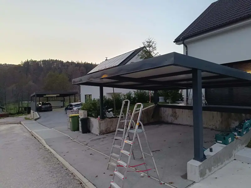 Kovinski nadstrešek za avtomobile ob hiši v večerni svetlobi